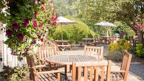 An outdoor patio with wooden tables and chairs, surrounded by lush greenery and flowering plants. - Holiday Inn Swindon by IHG (Swindon)