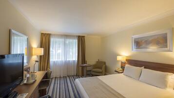 Une chambre d’hôtel comprenant un lit, un bureau avec une télévision, une chaise, une petite table et une lampe.