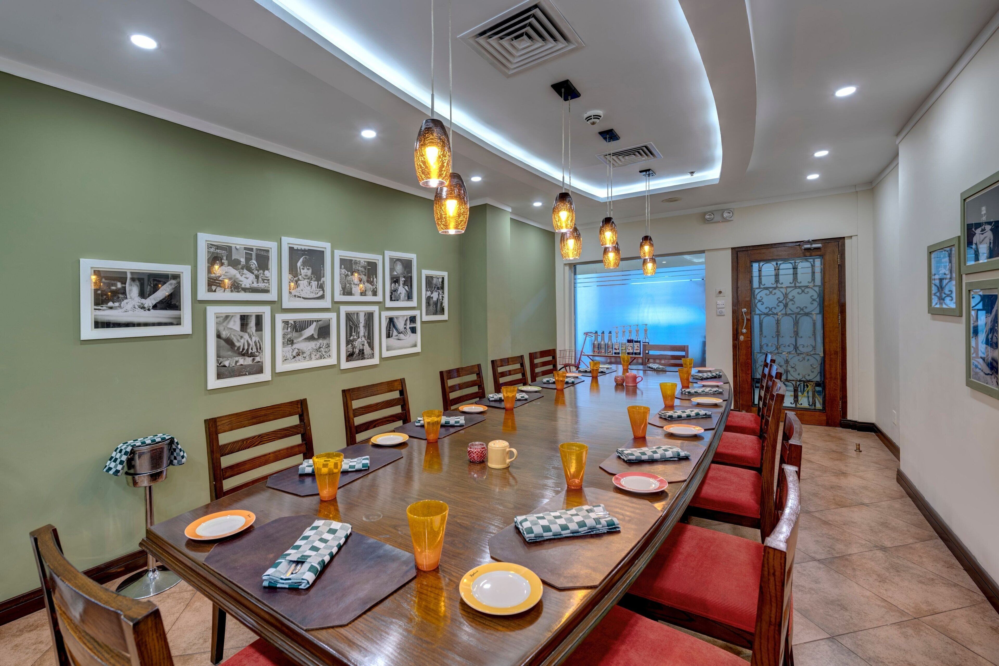 A long dining table with chairs, framed pictures on the wall, and pendant lights.