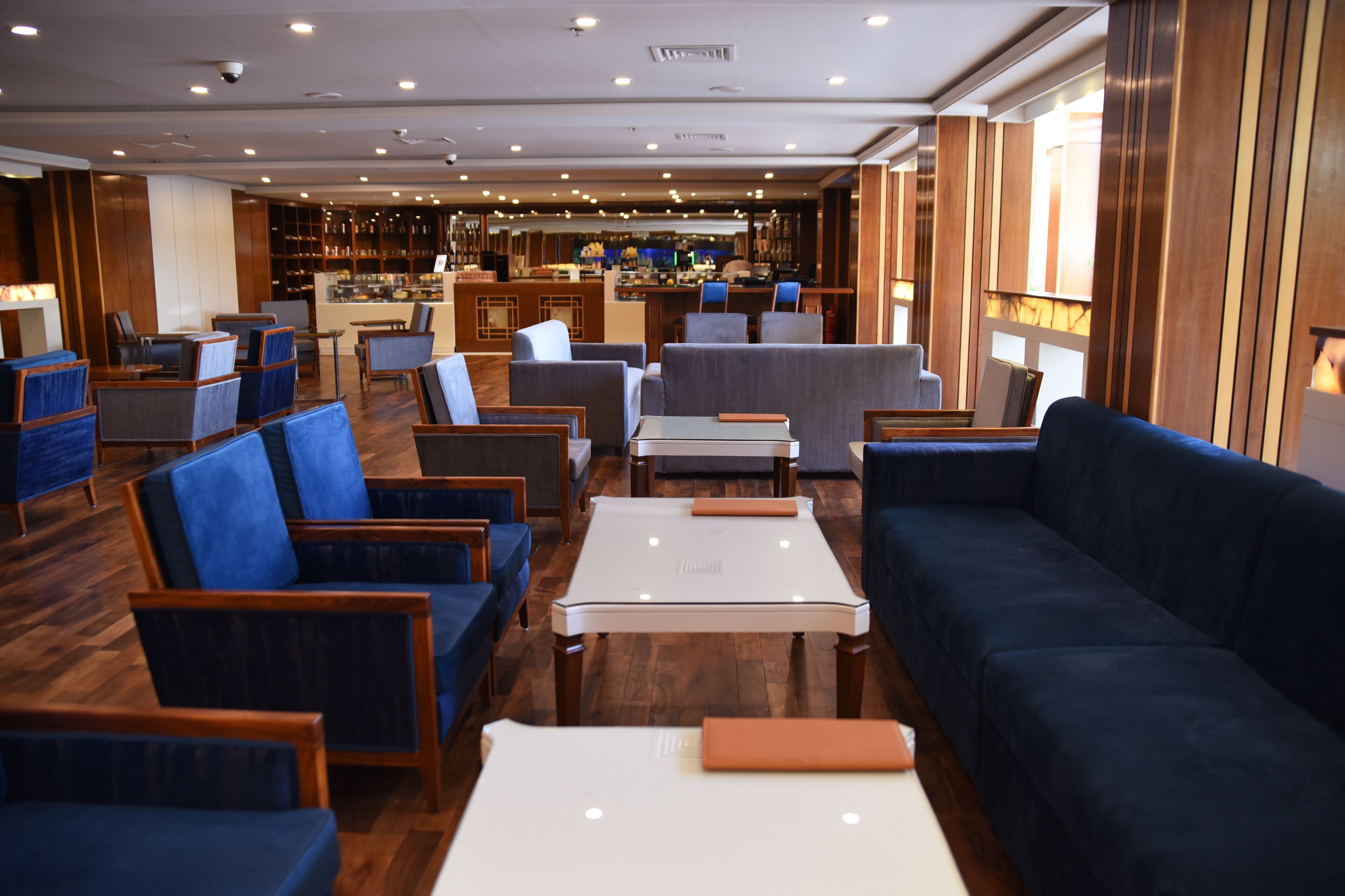 A modern lounge area with seating arrangements, a bar in the background, and wooden paneling on the walls.