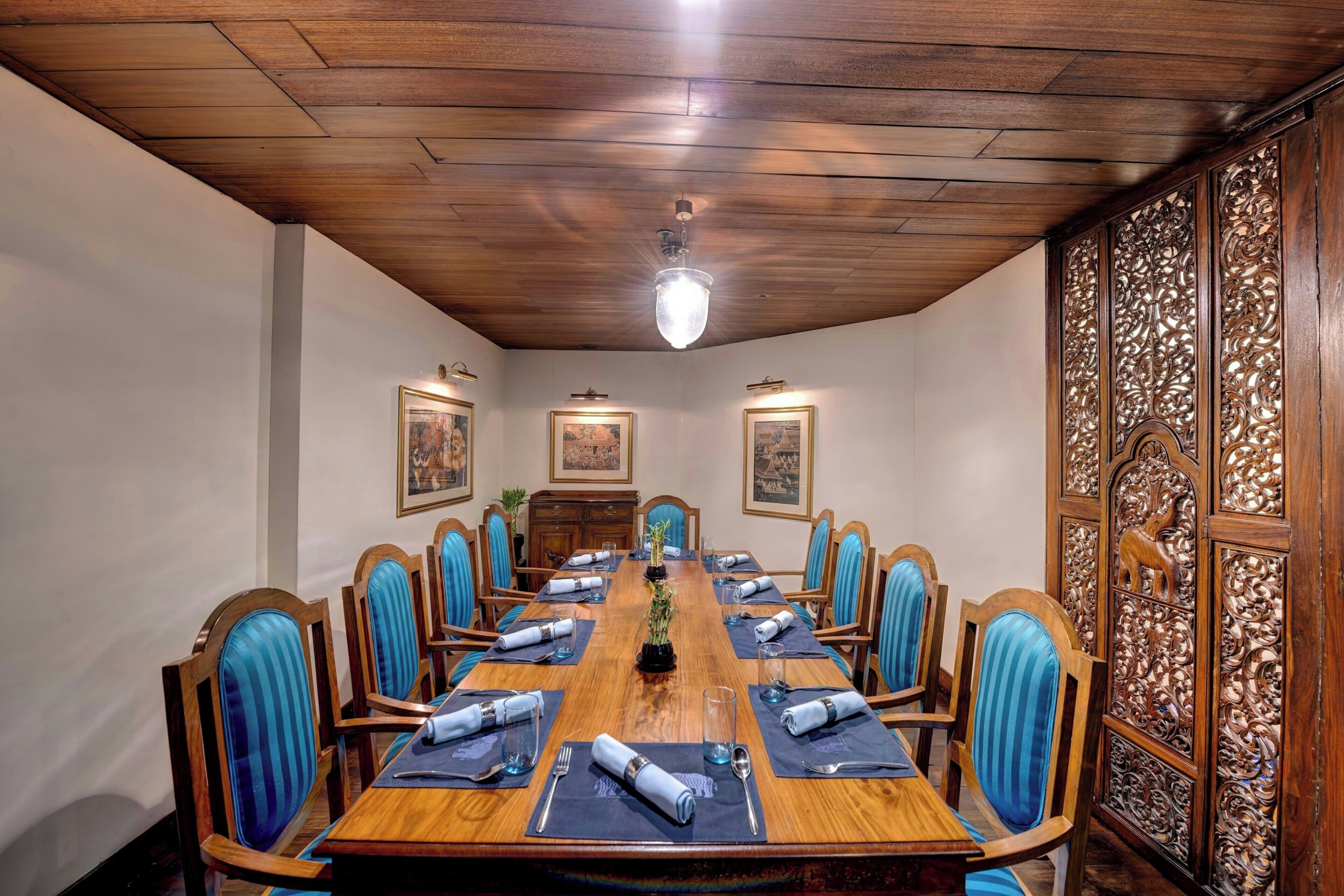 A conference room with a long table, blue-striped chairs, and framed pictures on the walls.