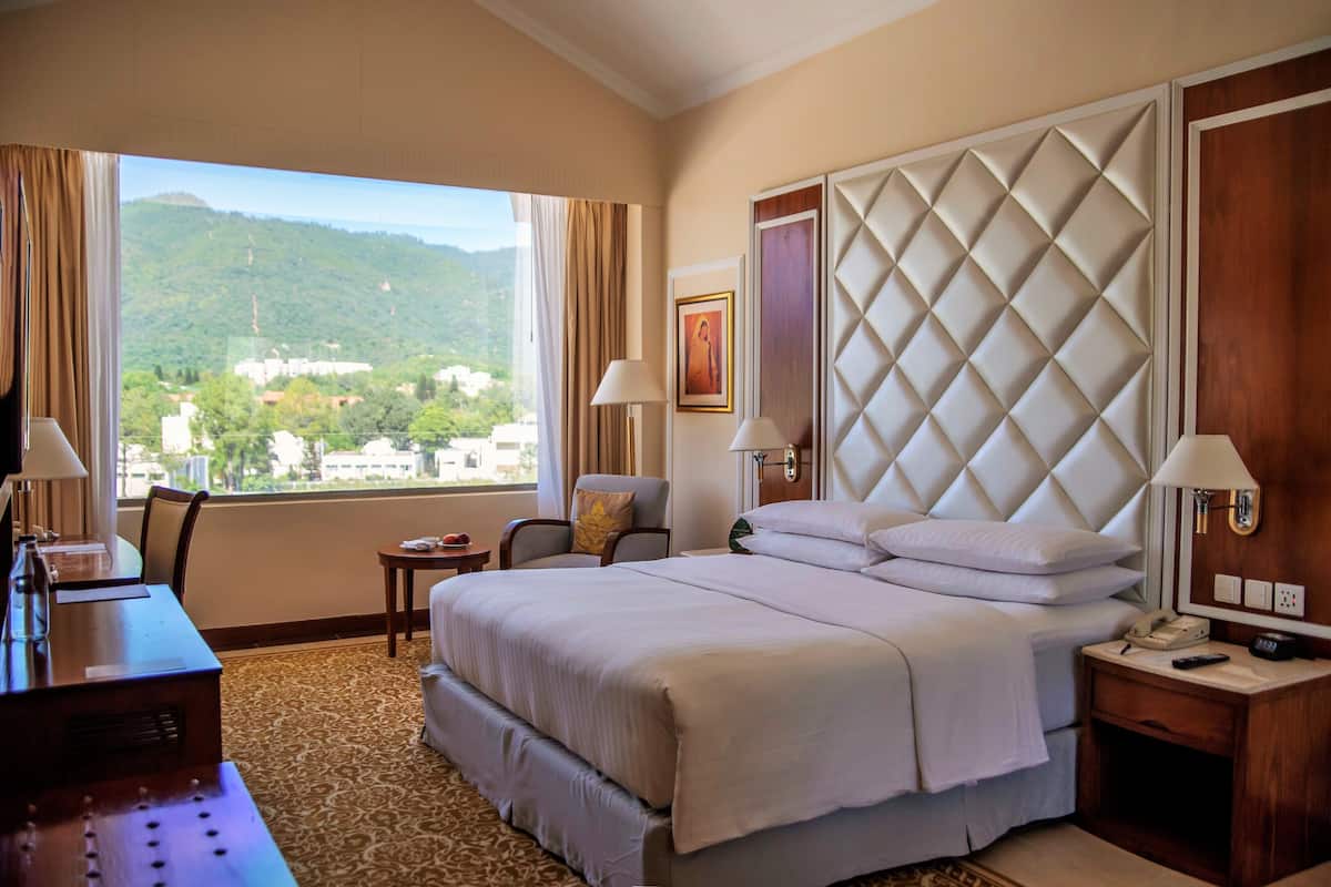 Habitación de hotel con una cama grande, un escritorio, una silla, una mesita y vistas a un paisaje montañoso.