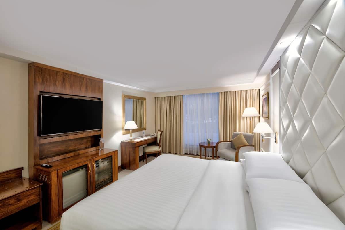 Una habitación de hotel con una cama grande, un escritorio con silla, televisión y minibar.