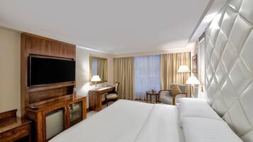 A hotel room with a large bed, a desk with a chair, a television, and a minibar.