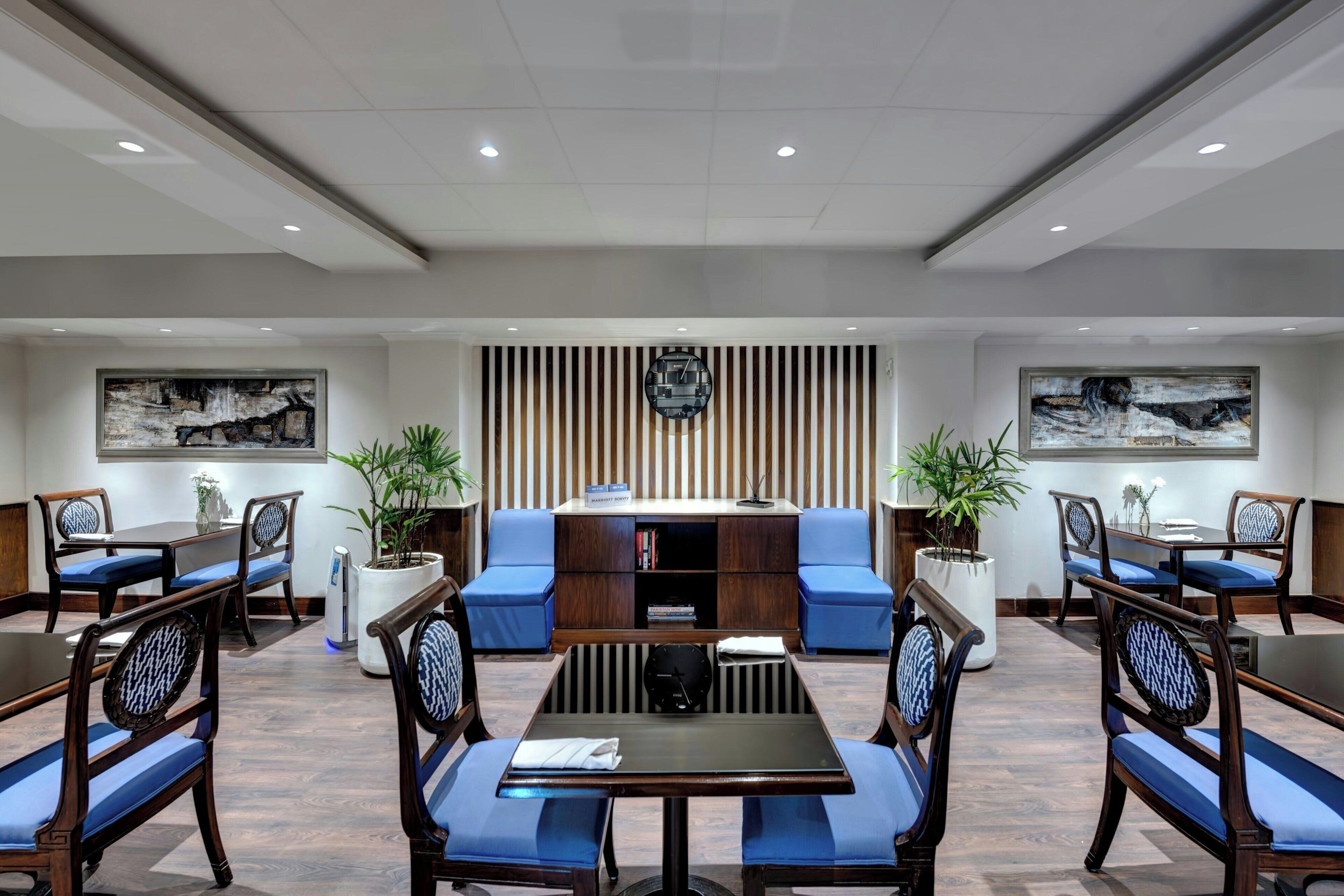 A conference room with a central table, blue cushioned seating, a clock, and a bookshelf.