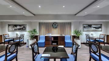 A conference room with a central table, blue cushioned seating, a clock, and a bookshelf.