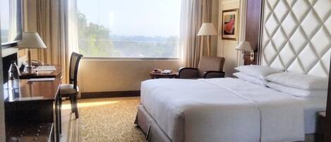 Habitación de hotel con una cama grande, un escritorio con lámpara, una silla y vista a la ciudad por la ventana.