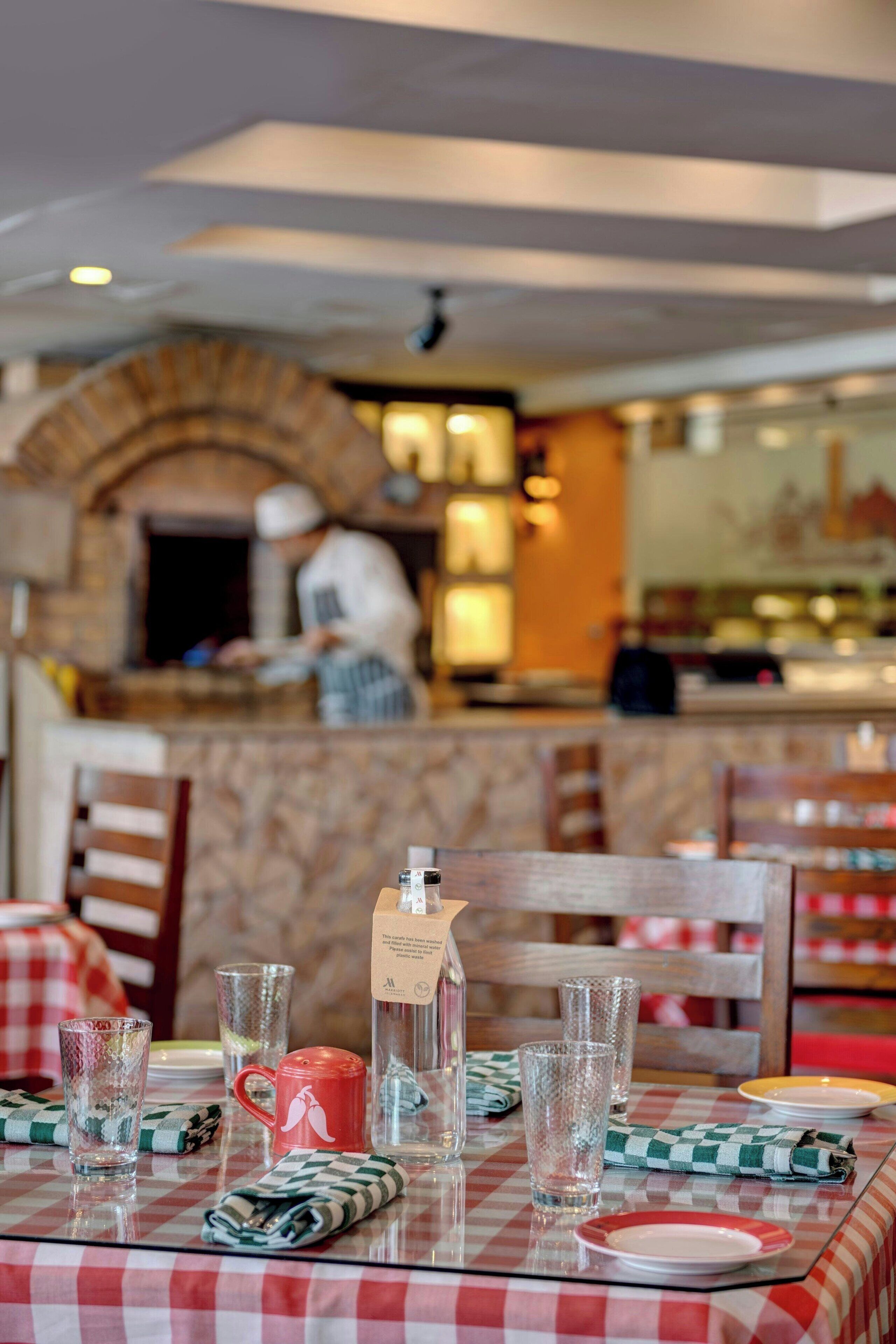 A restaurant interior with a checkered tablecloth, glasses, a mug, and a bottle on the table.