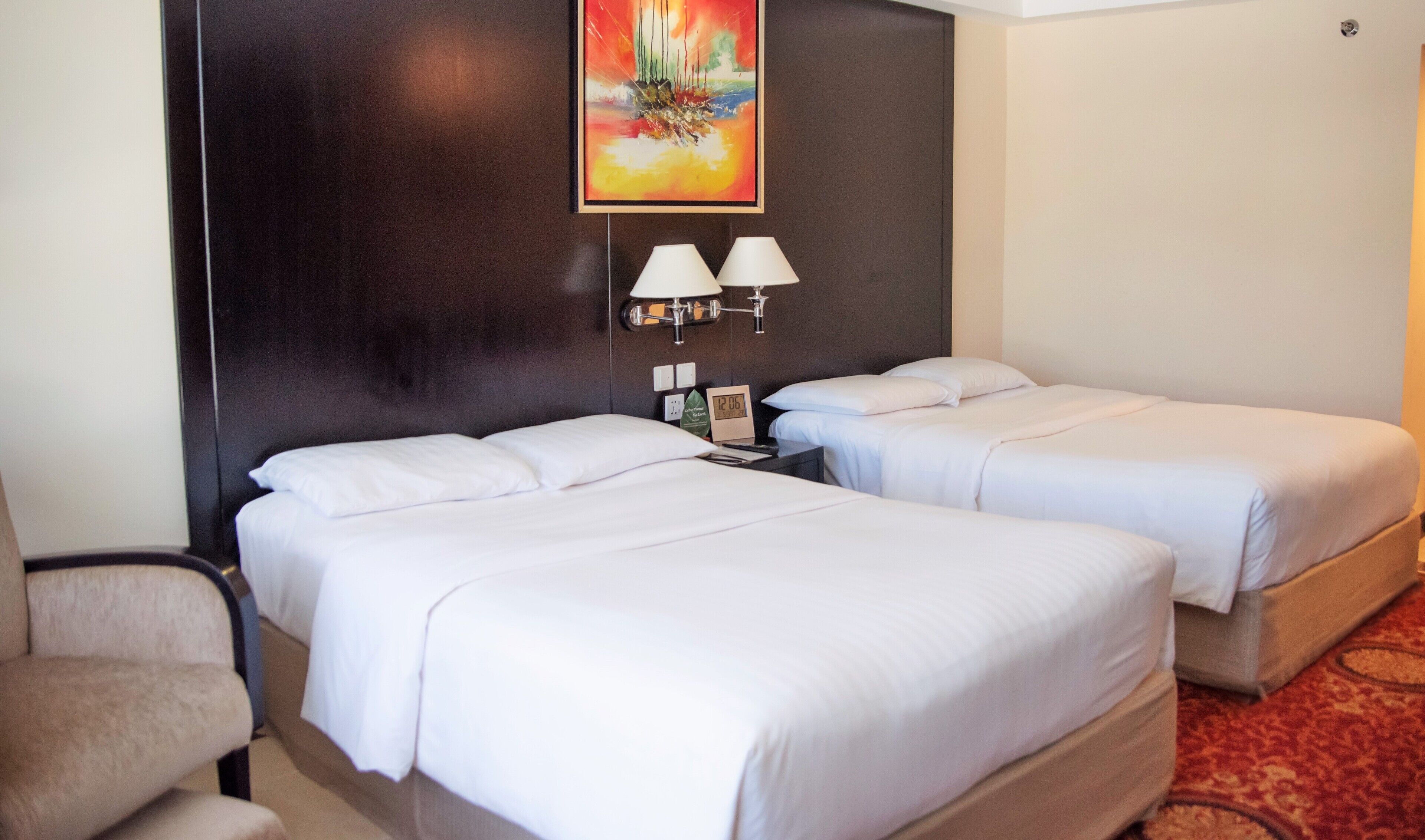 A hotel room with two beds, a painting on the wall, two bedside lamps, and a clock.