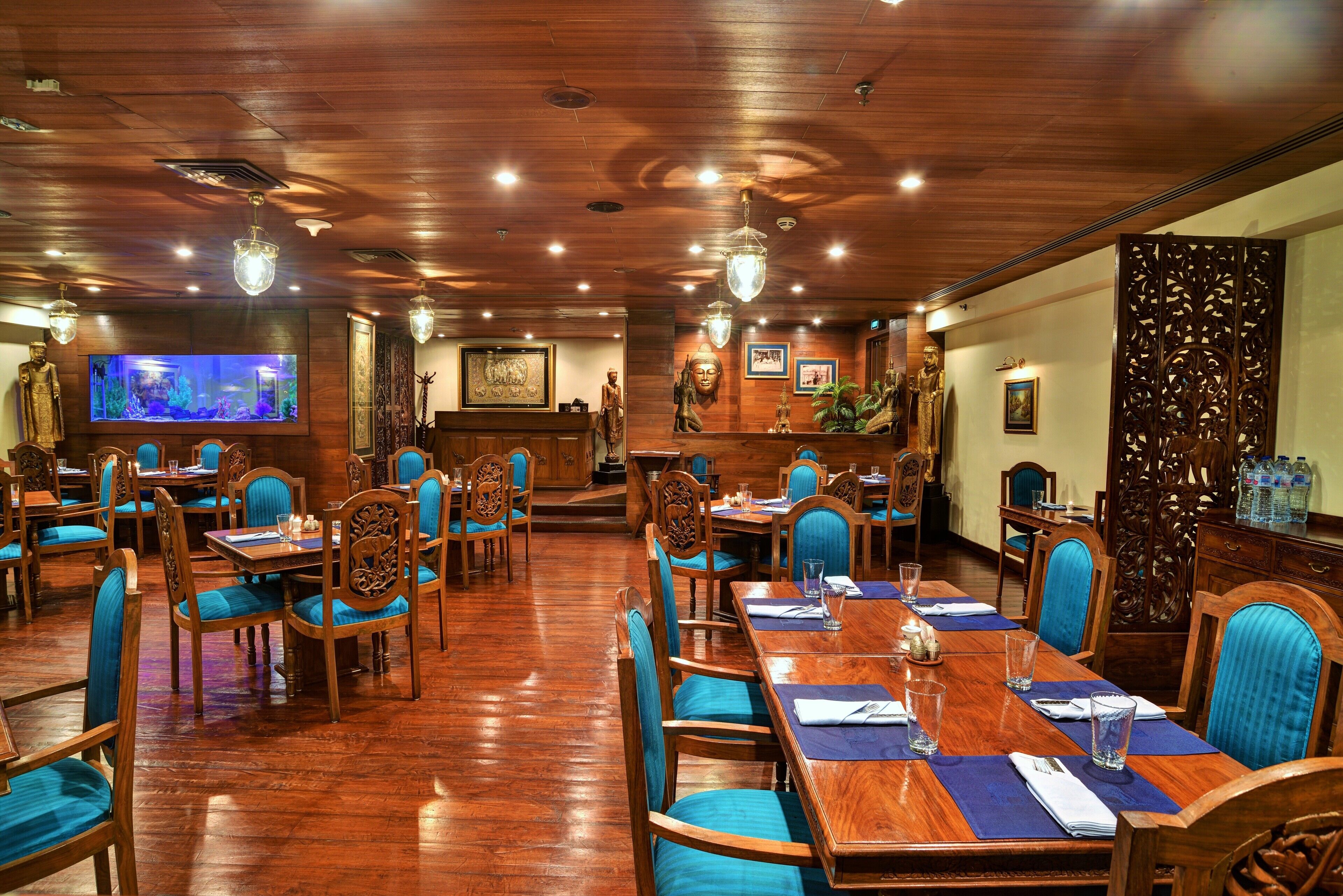 A restaurant with wooden floors and blue upholstered chairs. Tables are set with blue placemats and glassware.
