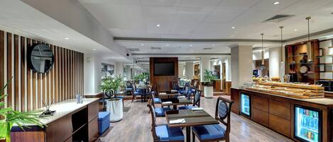Un moderno vestíbulo de hotel con paneles de madera, un mostrador de recepción, zonas de estar y un bar.
