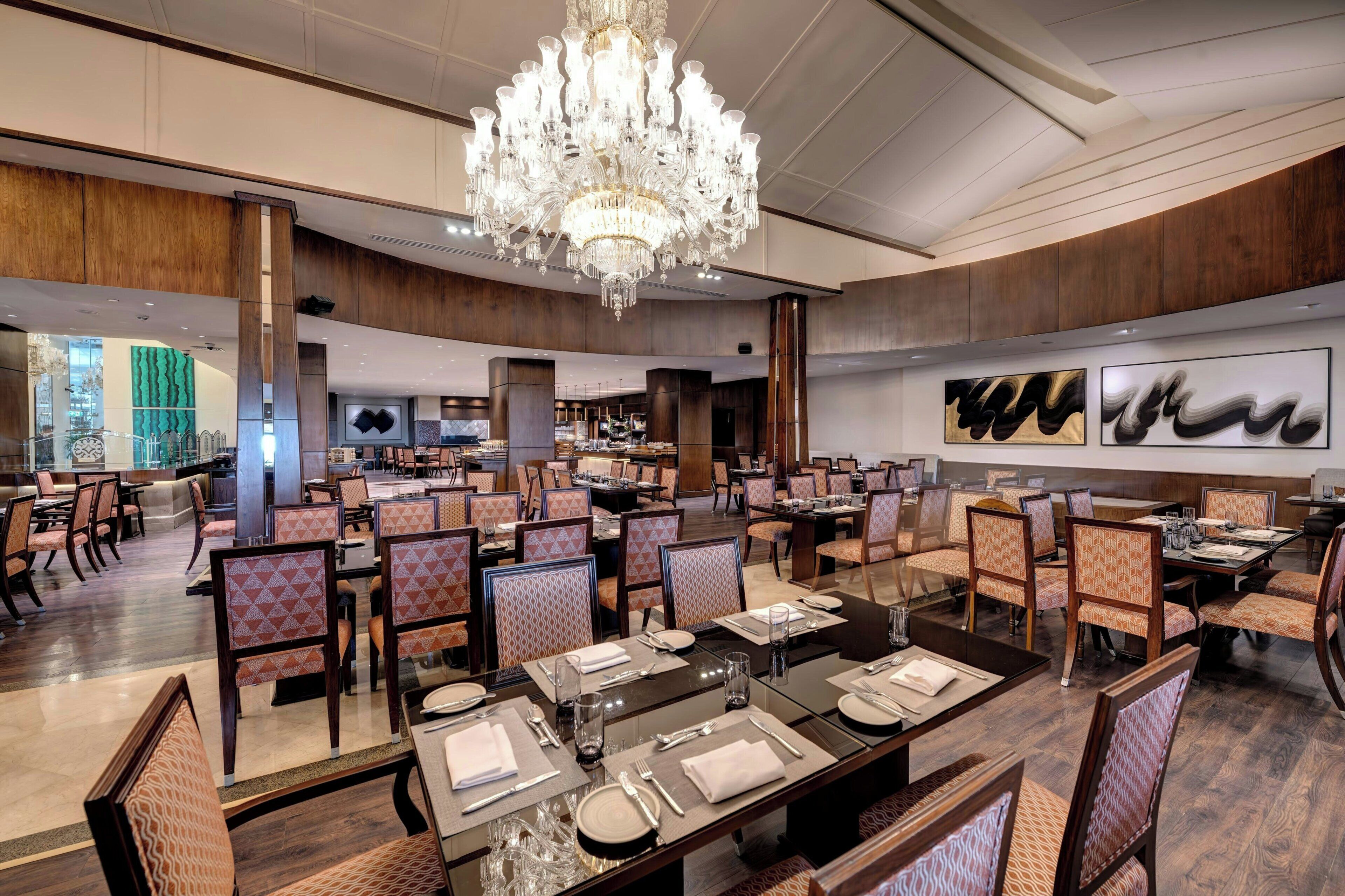 A spacious dining area with multiple tables and chairs, a large chandelier, and modern decor.