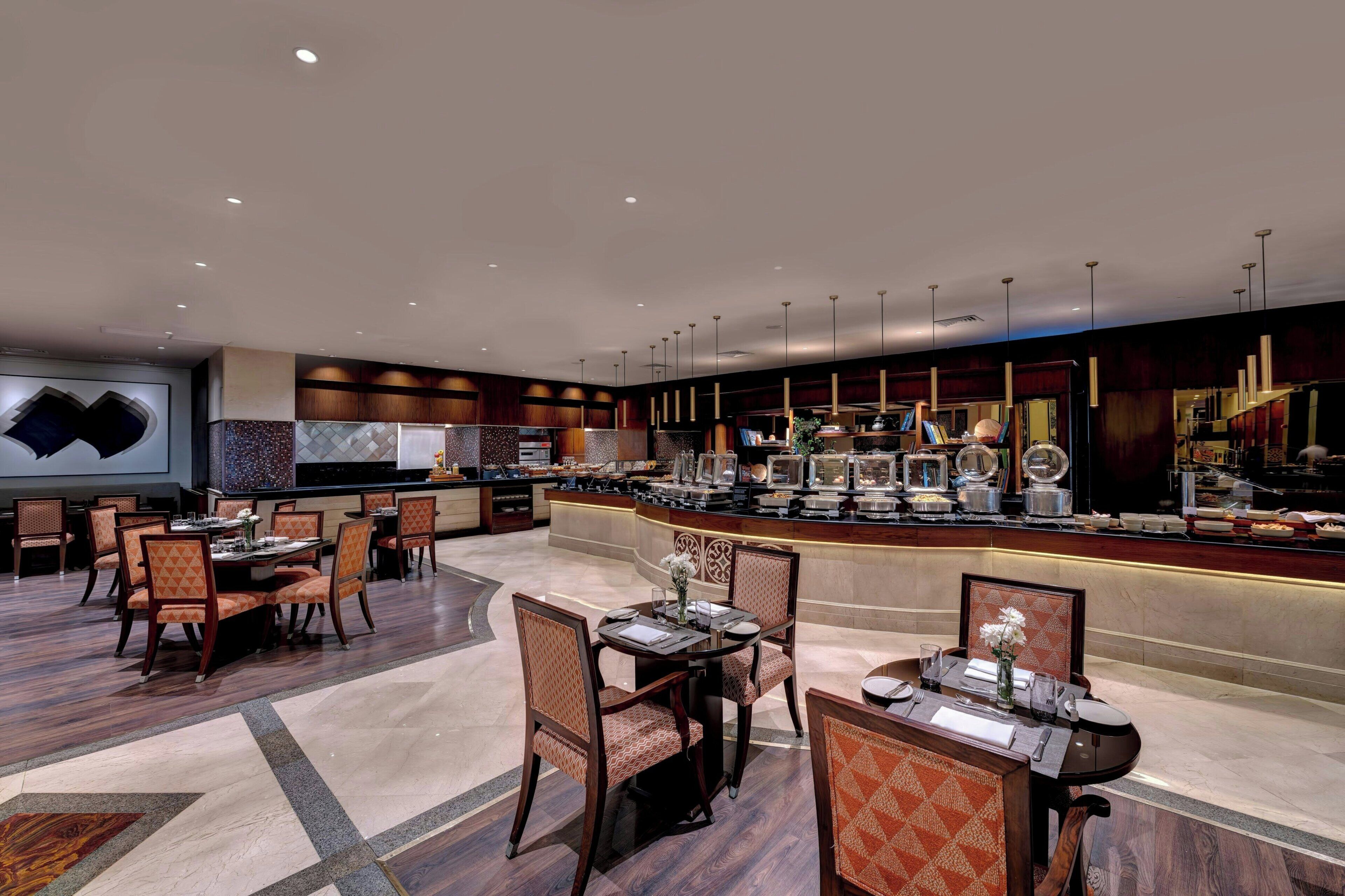 Una hall d'hotel con diversi tavoli da pranzo, sedie, una reception e un'area buffet.