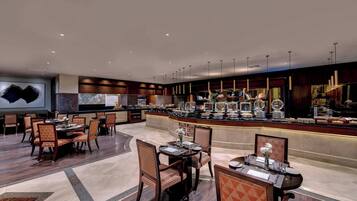 A hotel lobby with multiple dining tables, chairs, a reception desk, and a buffet area.