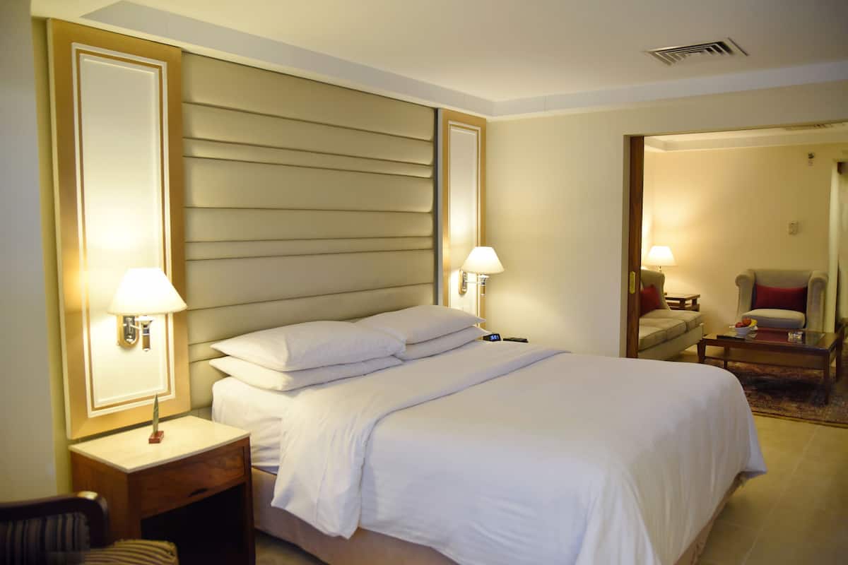 Una habitación de hotel con una cama grande, dos mesitas de noche con lámparas, una silla y una pequeña mesa con una lámpara.