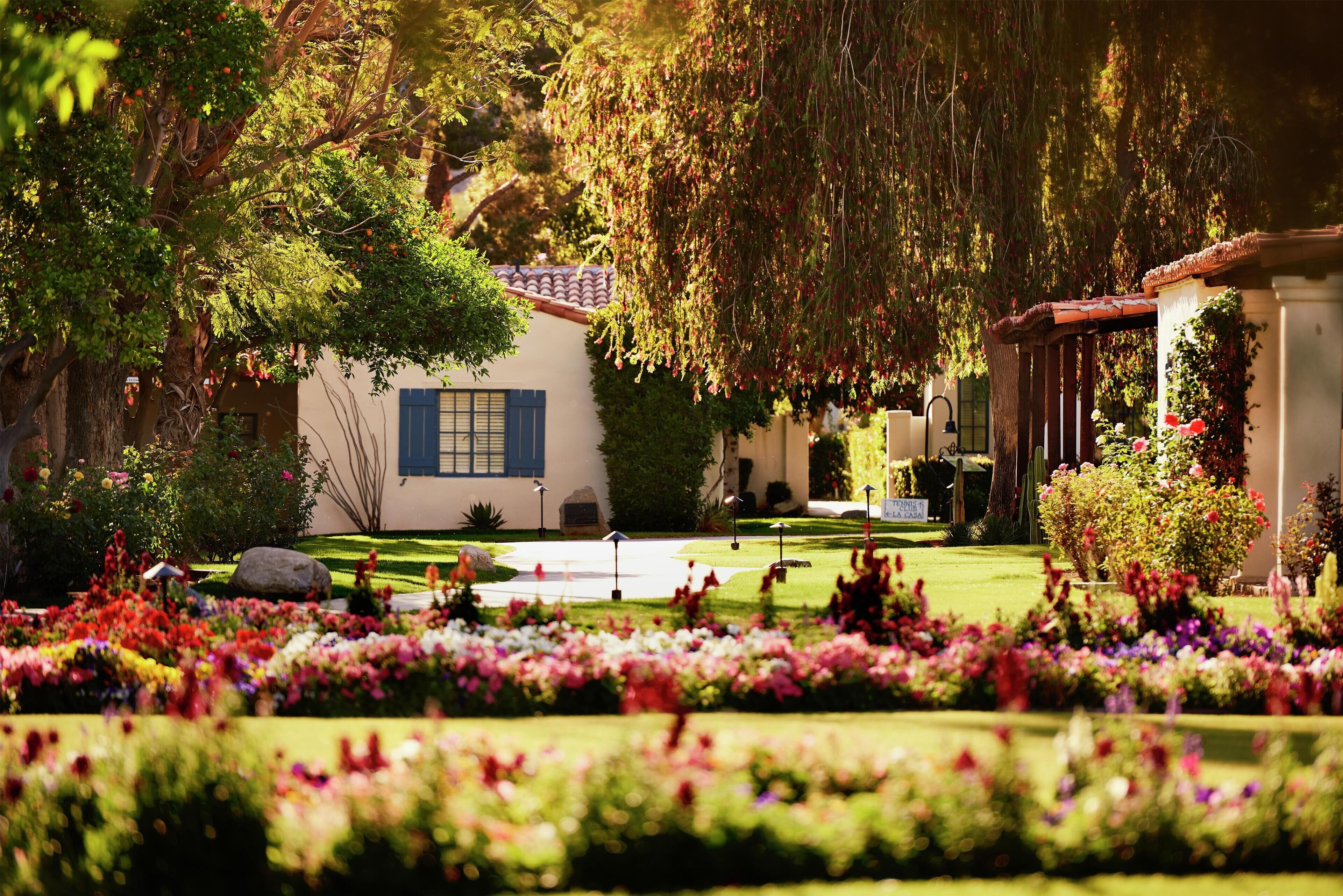 A well-maintained garden with a variety of colorful flowers and a house with a tiled roof and blue shutters.