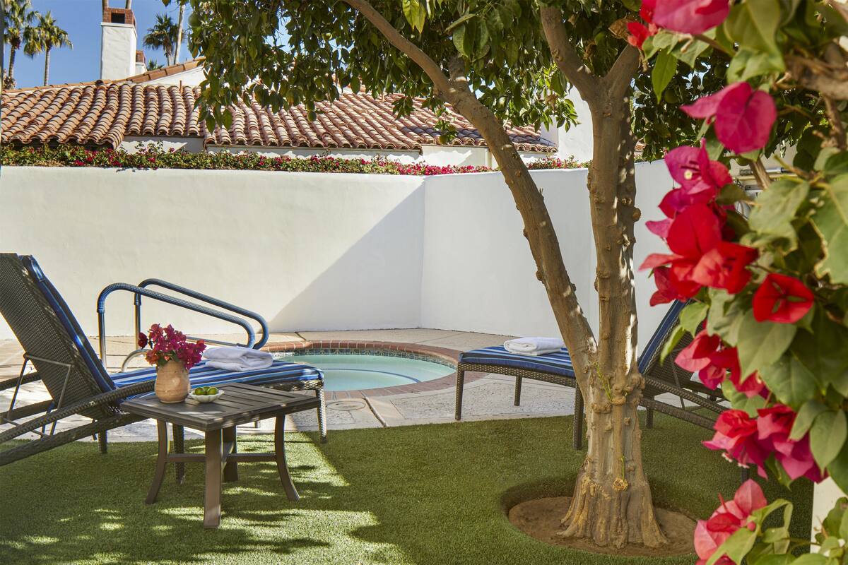 A poolside area with two lounge chairs, a small table with a vase of flowers, and a tree with pink flowers.