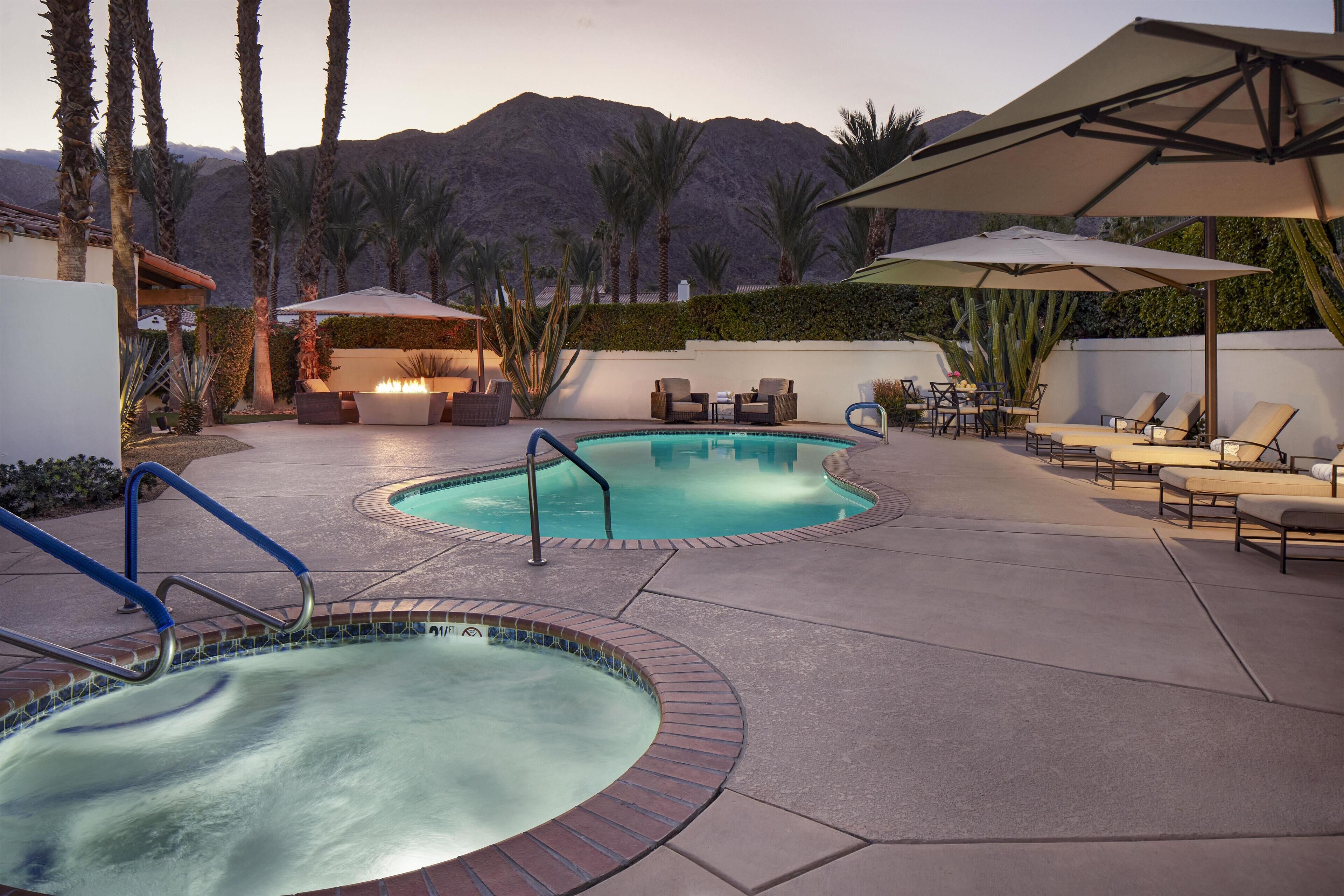 A pool area with two hot tubs, lounge chairs, and umbrellas.