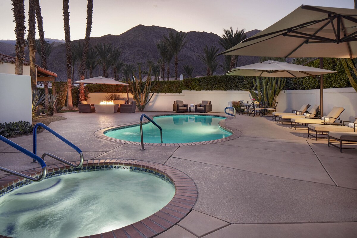 A pool area with two hot tubs, lounge chairs, and umbrellas.