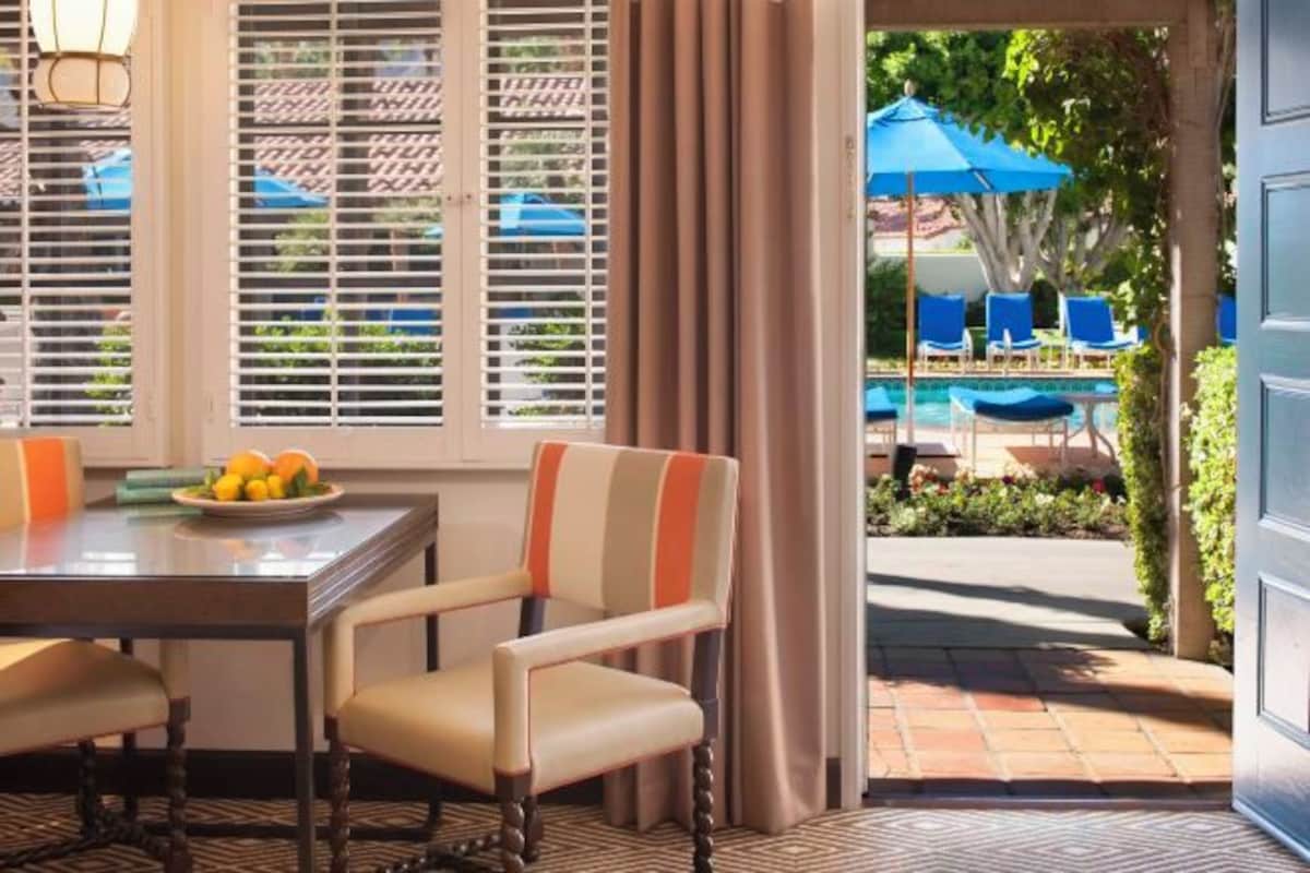 Un comedor con mesa y sillas, vista a una piscina con sombrillas, y una puerta que da a un espacio exterior.