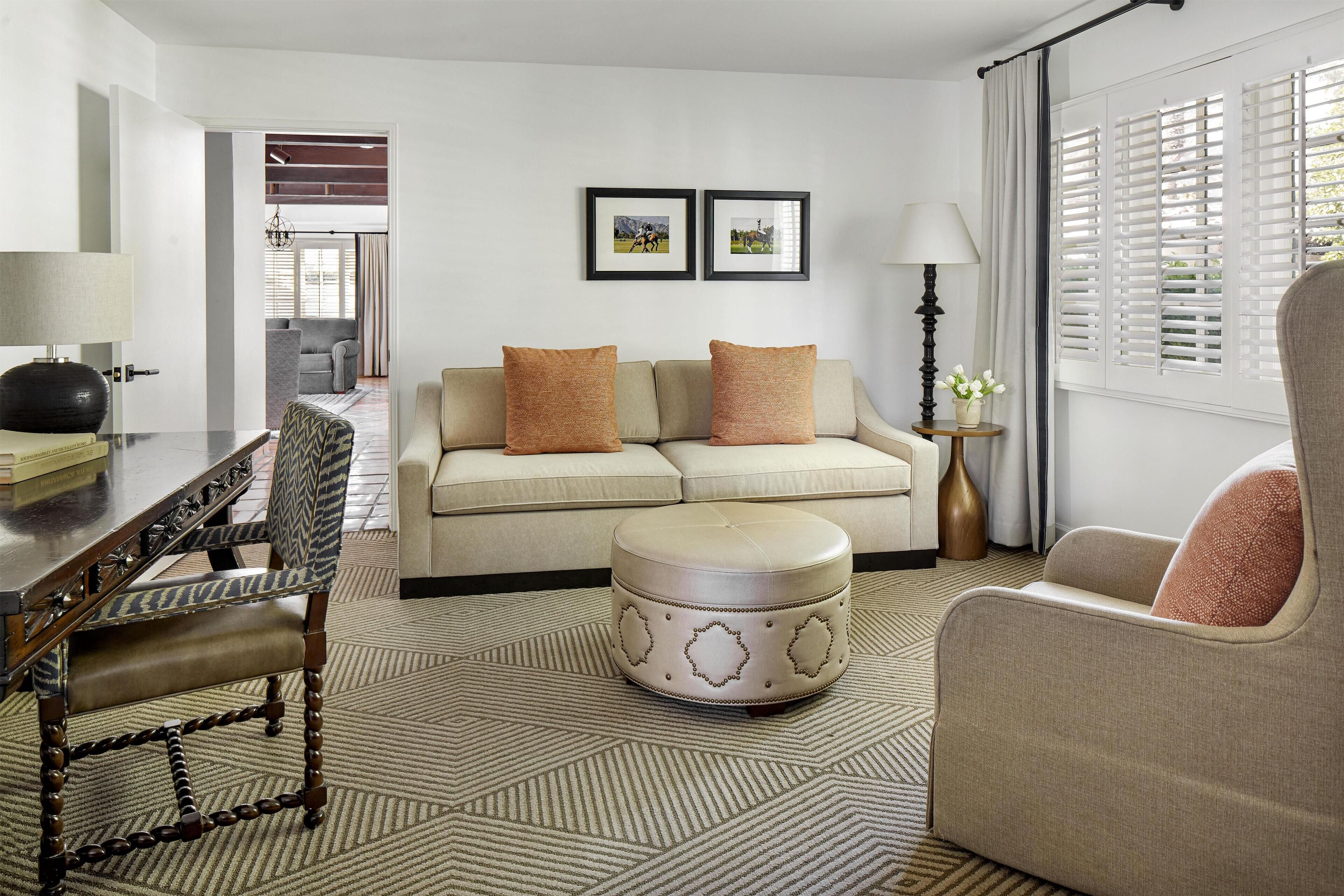 A modern living room with a sofa, ottoman, and armchair, a dining table, and a lamp.