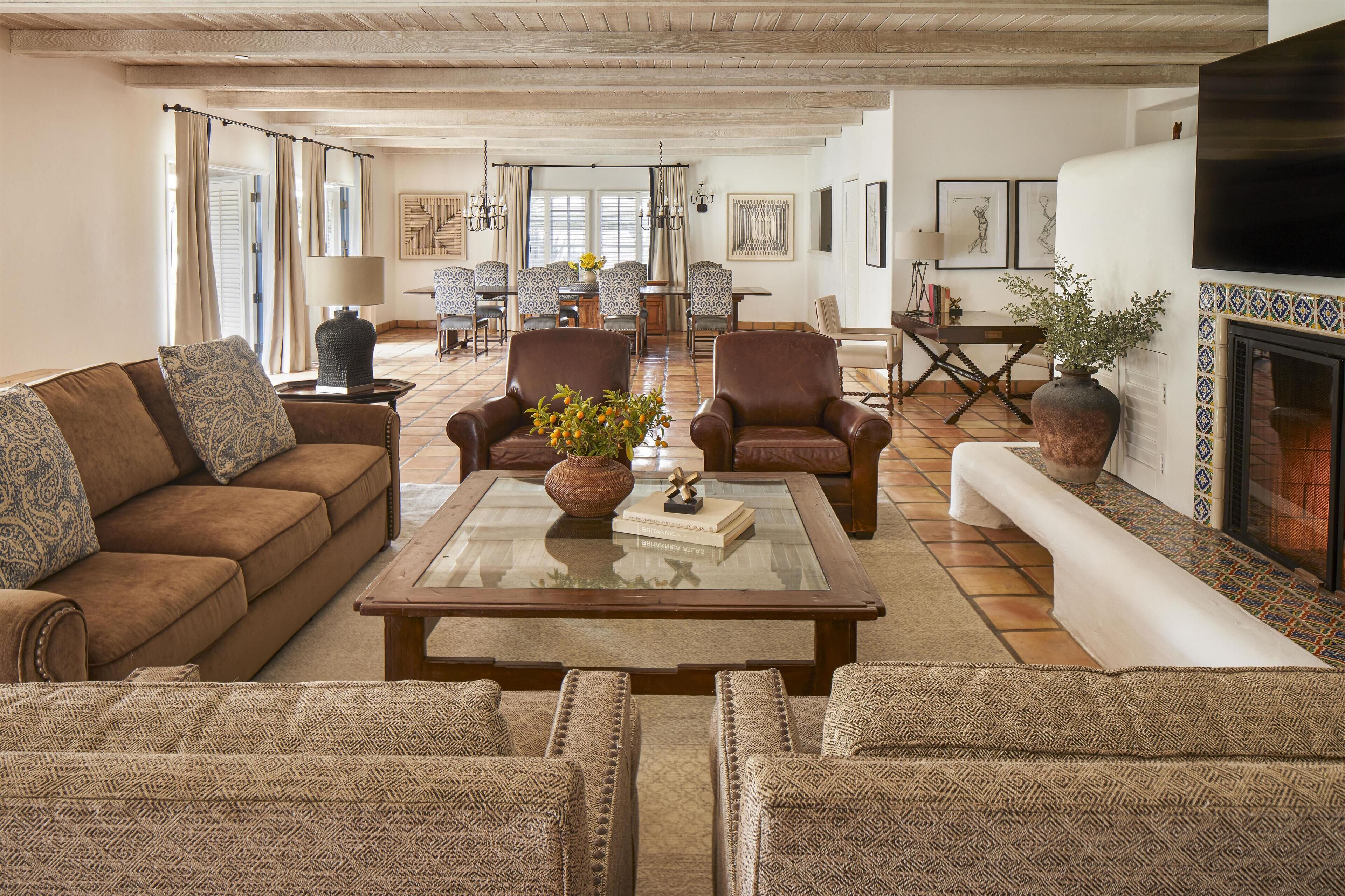 A spacious living room with a brown sofa, two armchairs, a glass coffee table, and a fireplace.