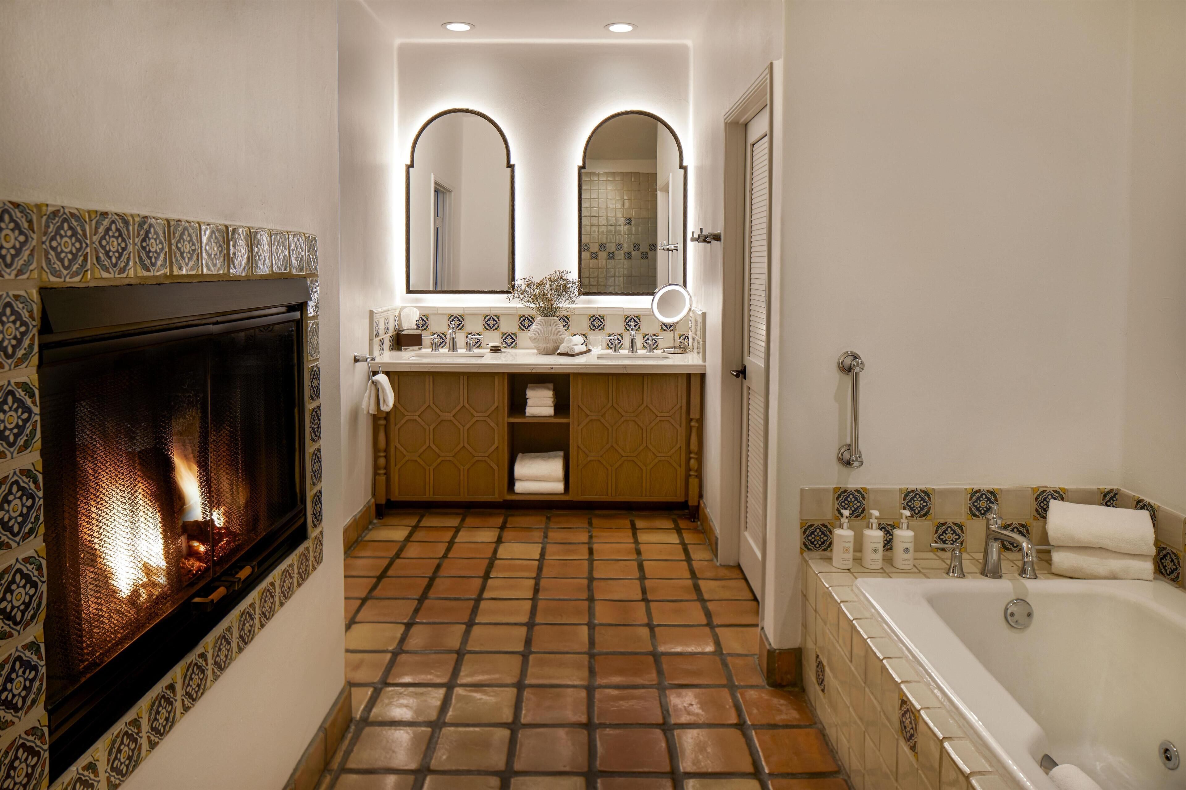 A bathroom with a fireplace, a bathtub, and a vanity with a mirror.