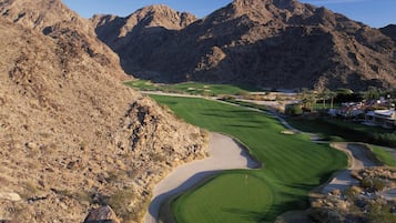 A golf course with a mountainous backdrop, well-maintained greens, and a clear sky.