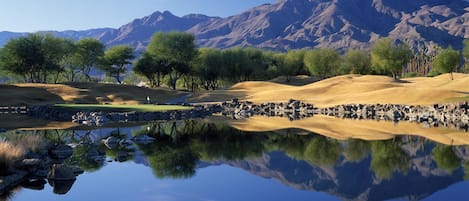 A serene landscape with a reflective pond, trees, and a mountain range in the background.