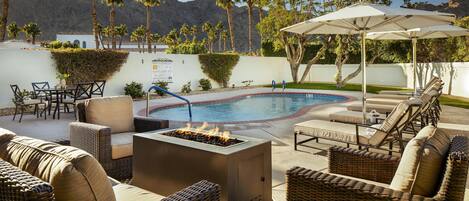 Un espace aménagé au bord de la piscine, avec des meubles en osier, un foyer et une vue sur les montagnes.