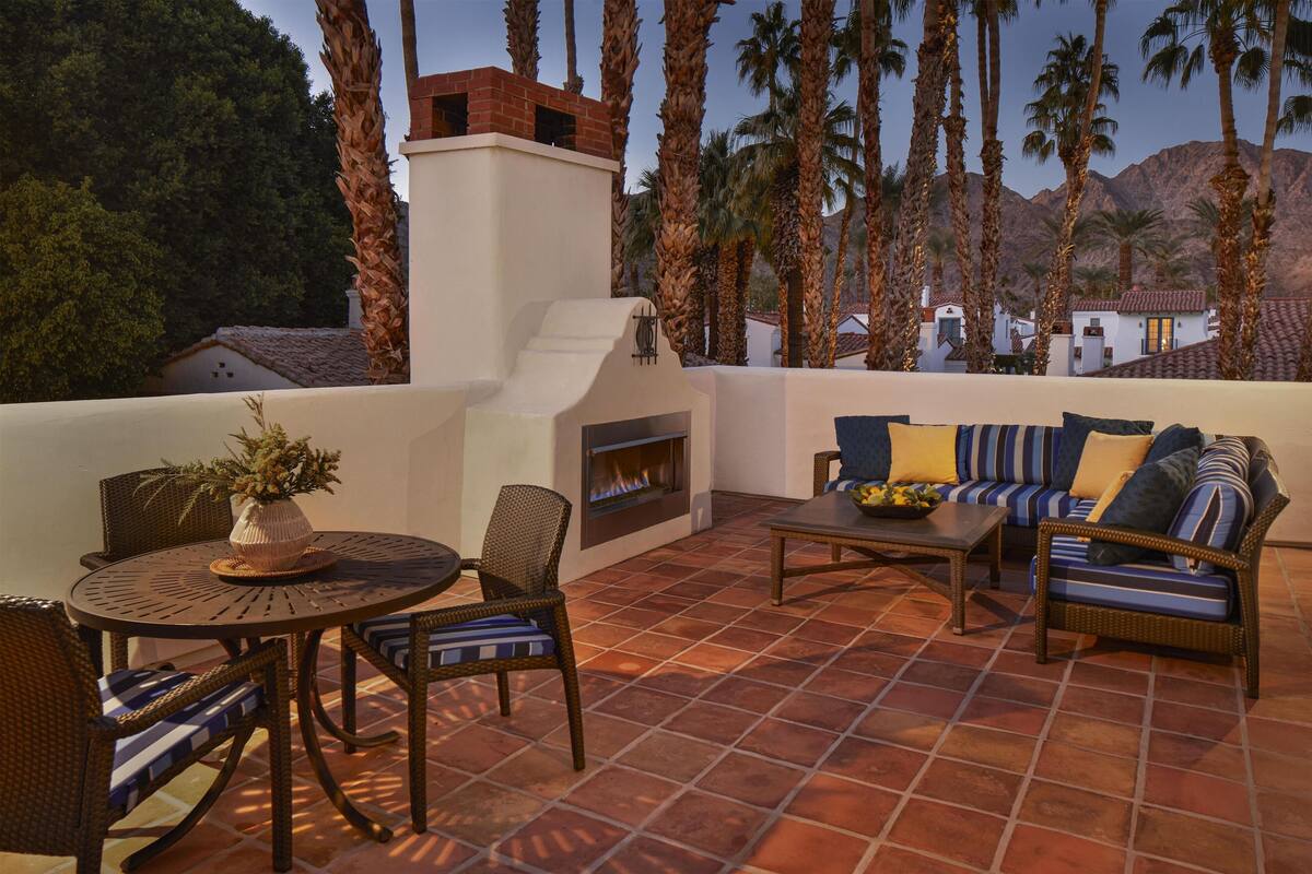 An outdoor patio with a round table, wicker chairs, a sofa, and a fireplace.