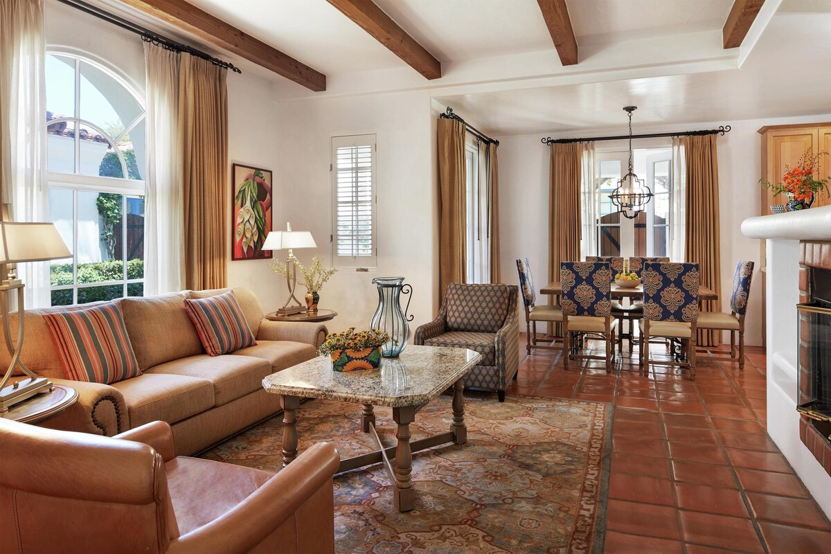 A living room with a sofa, armchairs, a coffee table, and a dining area with chairs and a table.
