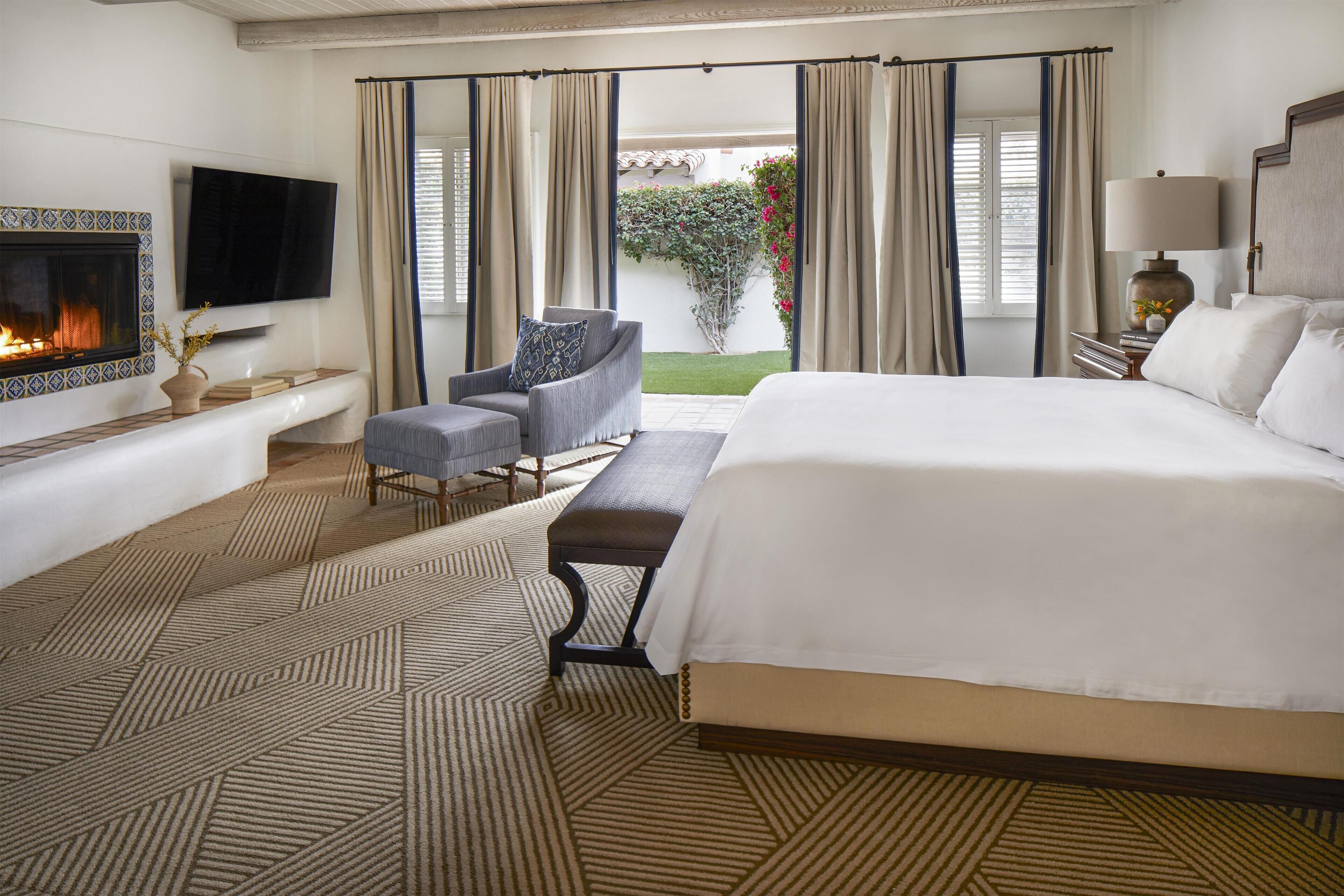 Une chambre d’hôtel avec un grand lit, un téléviseur fixé au mur, une cheminée, un banc et une vue sur l’extérieur.