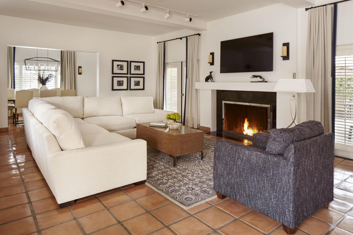 A living room with a sectional sofa, a gray armchair, a coffee table, a fireplace, and a flat-screen TV mounted above it.