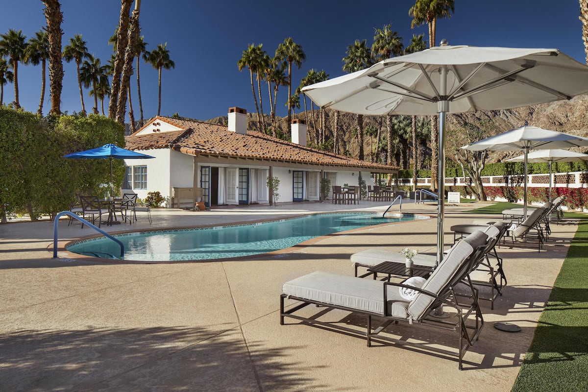 A pool area with lounge chairs, umbrellas, and a building with a tiled roof.