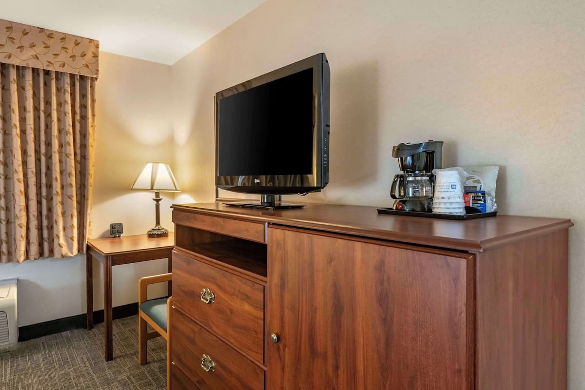 Ein Hotelzimmer mit Holzschreibtisch, Flachbildfernseher, Lampe, Kaffeemaschine und Schrank.