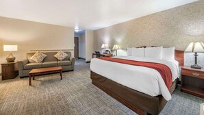 Habitación de hotel con una cama grande, un sofá, una mesa de centro y dos mesitas de noche con lámparas.