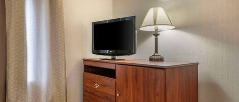 Una habitación de hotel con un mueble de madera, un televisor de pantalla plana, una lámpara y una cortina color beige.