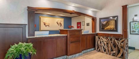 A reception area with a wooden reception desk, framed artwork, a potted plant, and a mounted television.