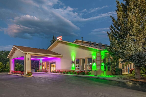 A motel with a covered parking area, a sign indicating 'Maverick', and a green-lit exterior.