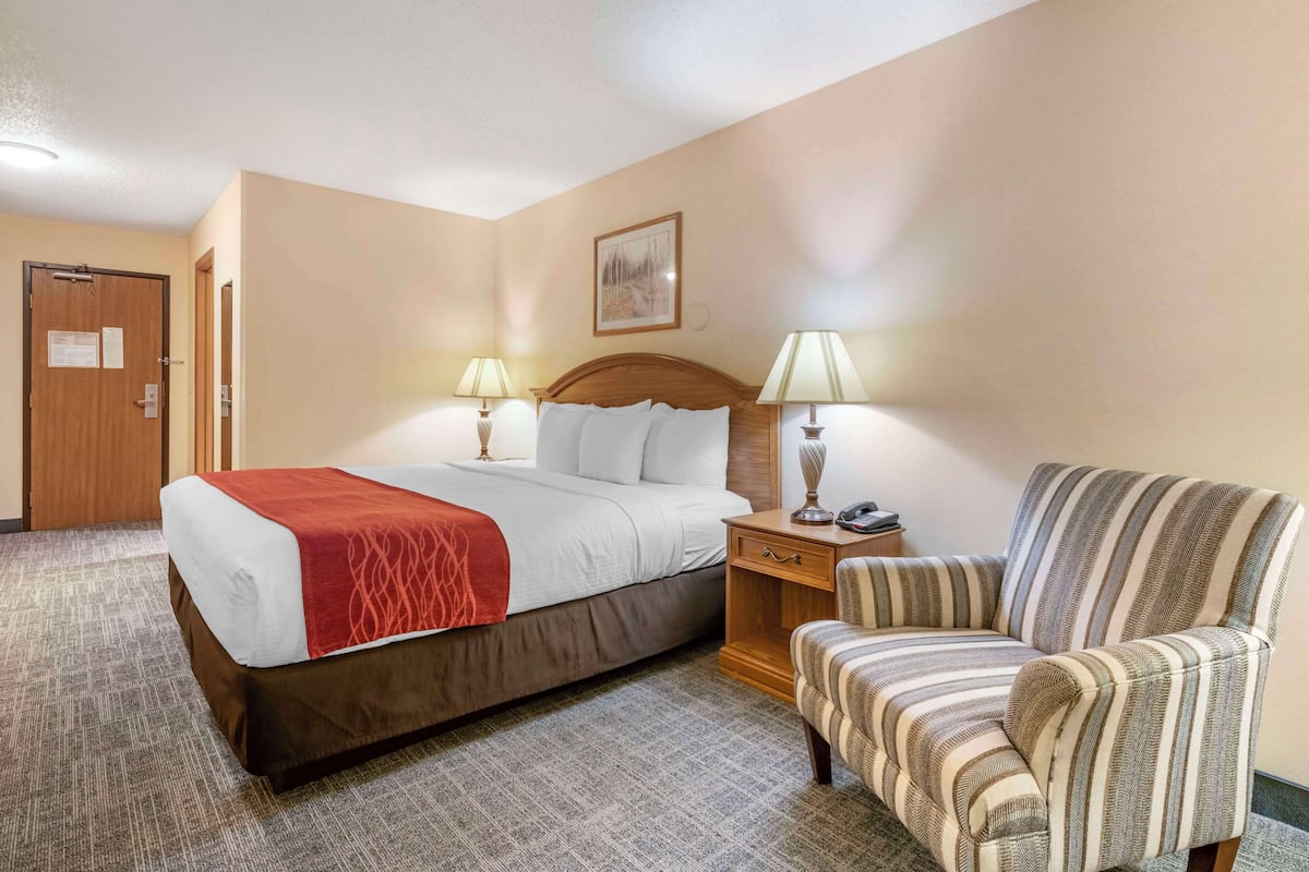 Ein Hotelzimmer mit einem Bett, zwei Nachttischlampen, einem Sessel und einer Tür.