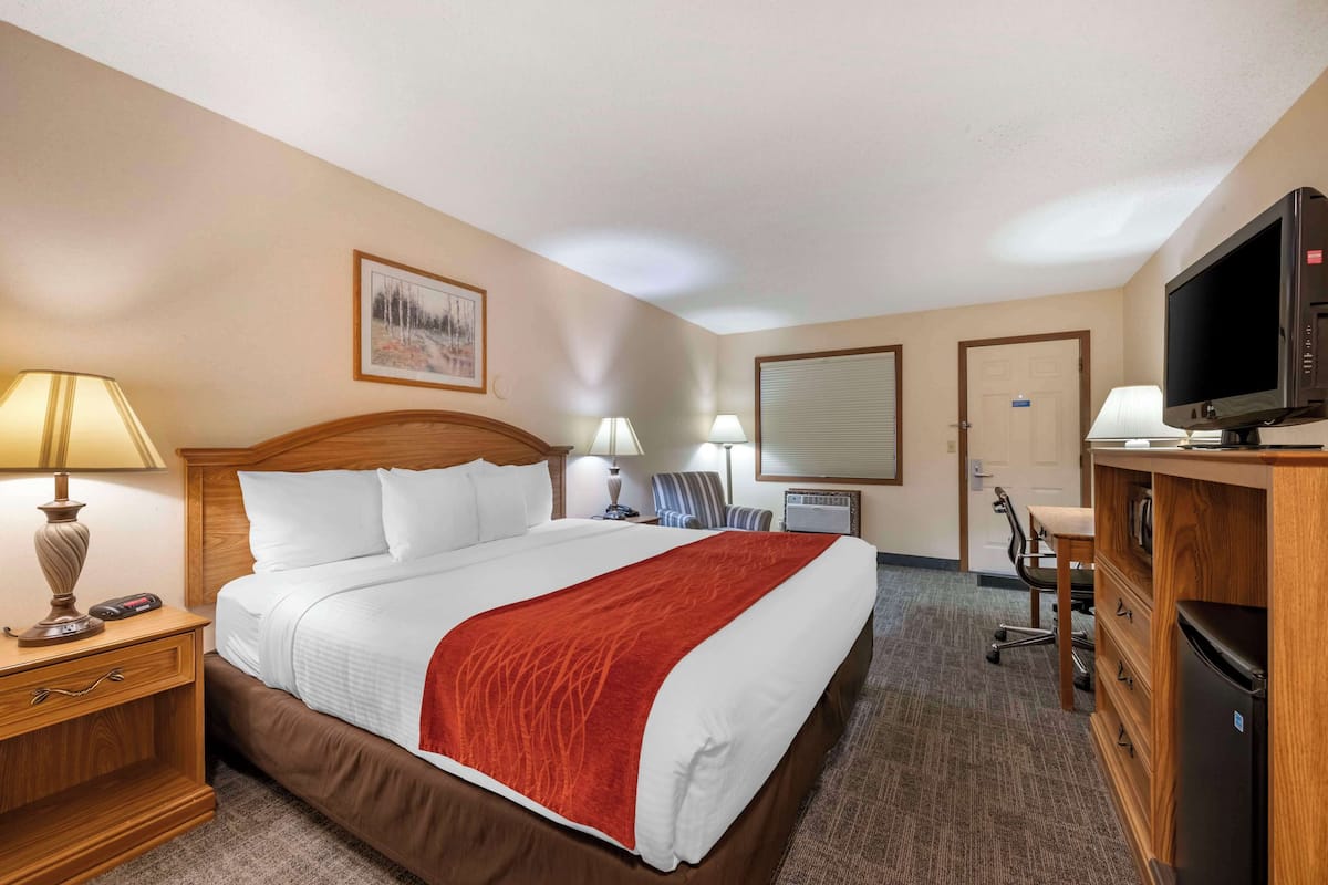 Ein Hotelzimmer mit einem großen Bett, einem Schreibtisch mit Computer, einem Fernseher und einem Sessel.