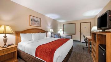 A hotel room with a large bed, a desk with a computer, a TV, and a chair.