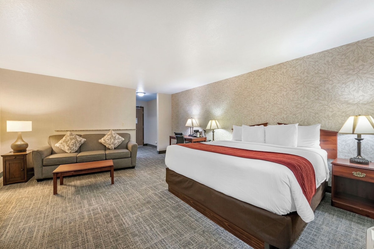A hotel room with a large bed, a sofa, a coffee table, and two lamps.