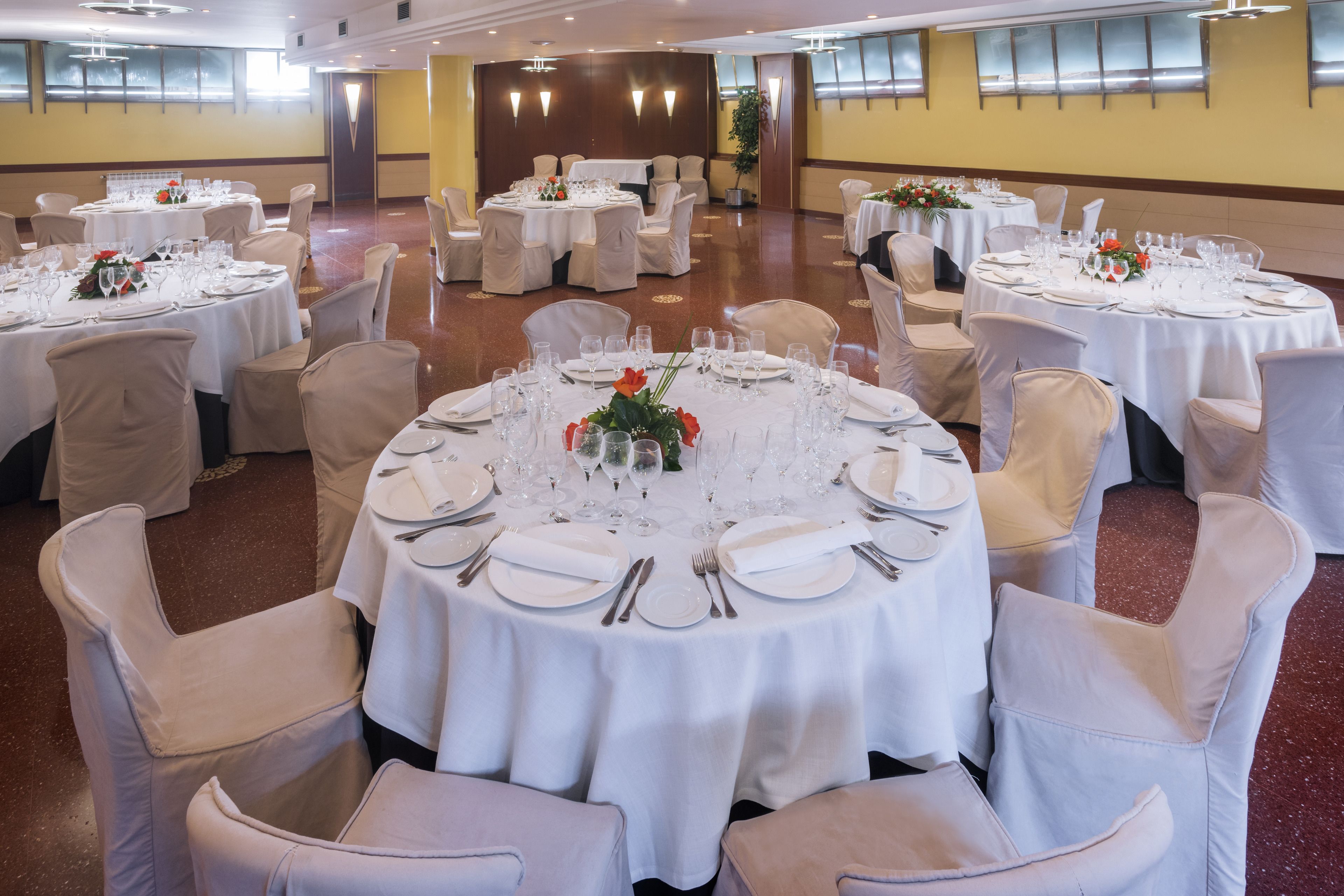 A banquet hall with round tables set for dining, each with white tablecloths and chairs.