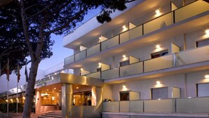 Un hotel moderno con una estructura de varios pisos, balcones de cristal y una entrada bien iluminada.