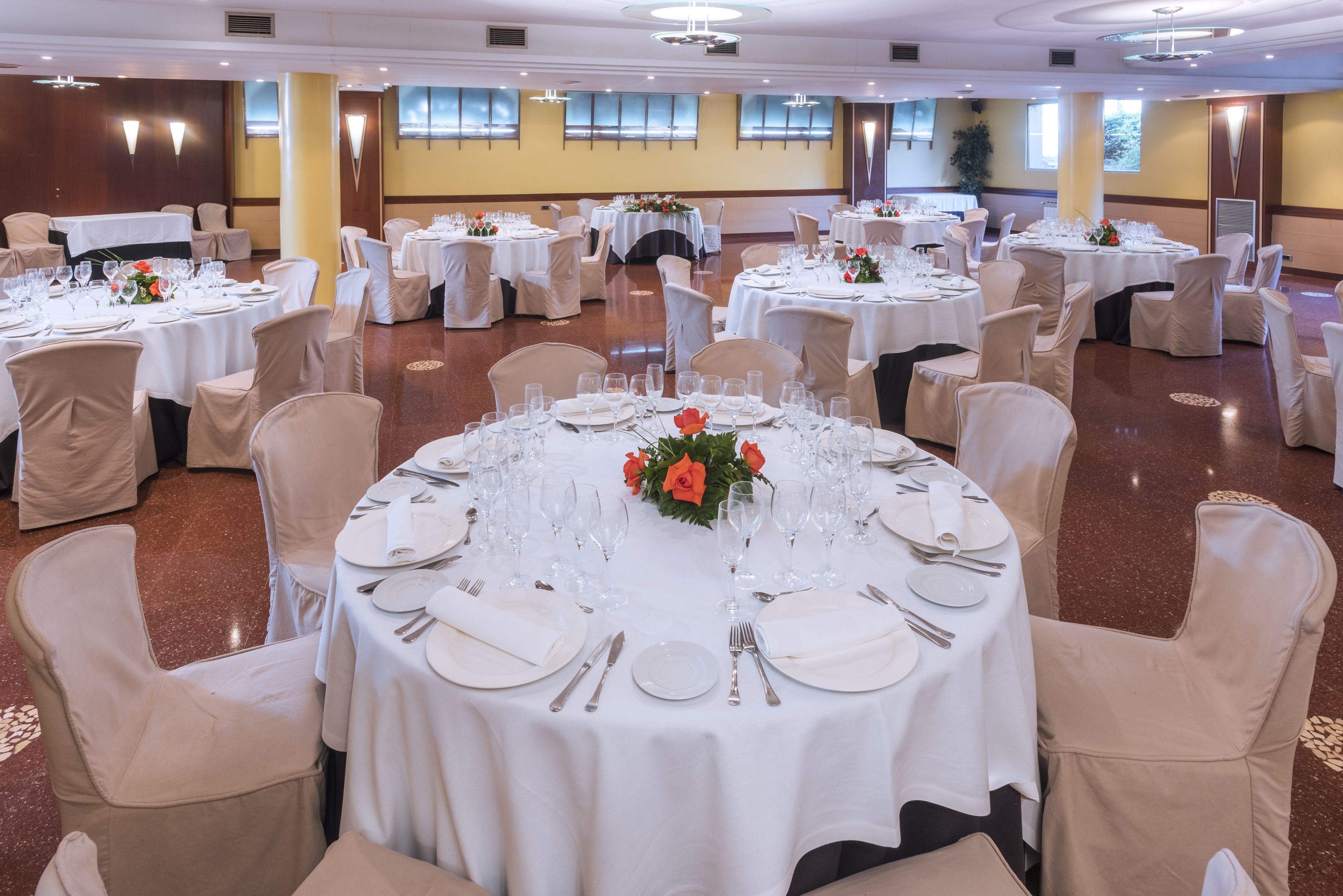 Un salón de banquetes con mesas redondas dispuestas para cenar, cada una con manteles blancos y centros de mesa florales.