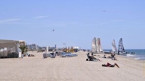 Una playa con tumbonas, sombrillas y veleros.