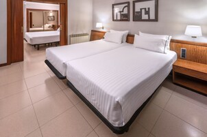 Una habitación de hotel con dos camas, cabecero de madera, lámparas de noche y un espejo.