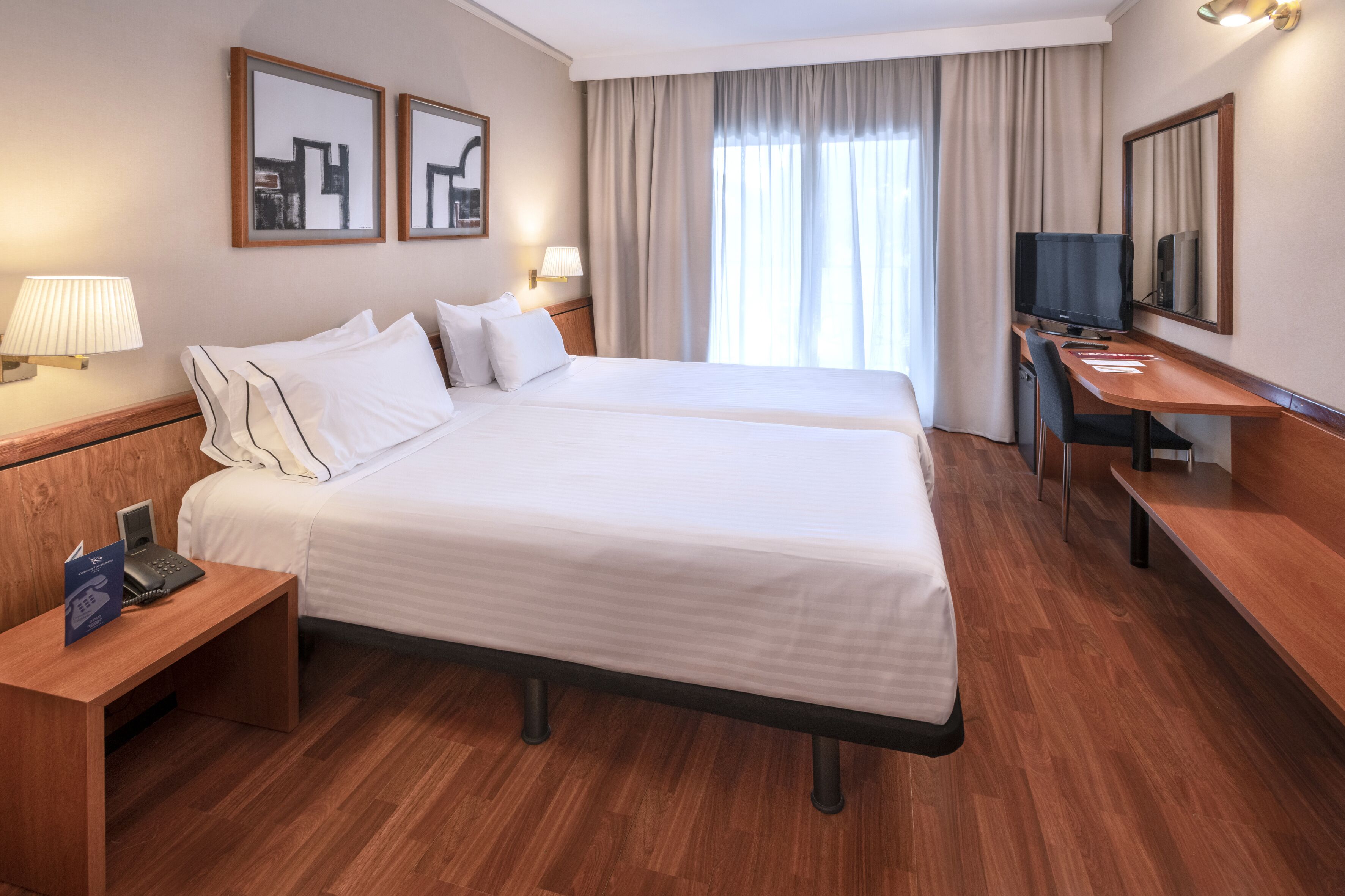 Habitación de hotel con dos camas, un escritorio, un televisor y un teléfono.